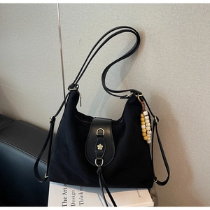 Detail of black suede hobo bag with metal flower buckle and beaded charm ornament
