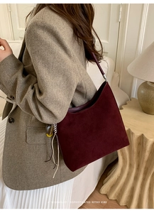 Close-up of minimalist burgundy suede bucket bag with smooth leather shoulder strap