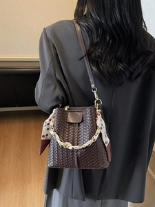 Deep brown woven bucket bag with silk scarf chain strap worn by a model in a suit