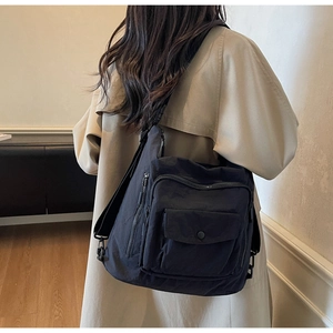 Detailed back view of a versatile black nylon crossbody bag worn by a model in a room