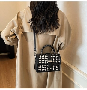 Detail view of woven top handle and silver H-buckle on black and white checkered bag