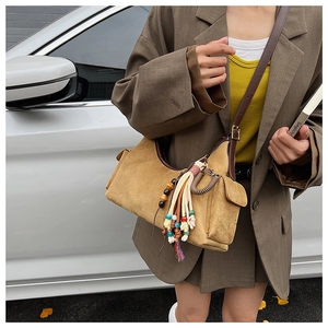 Detail of yellow suede crossbody bag with colorful tassel and adjustable brown leather strap