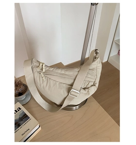 Detail of beige crescent shoulder bag with wide strap and silver hardware on wooden table