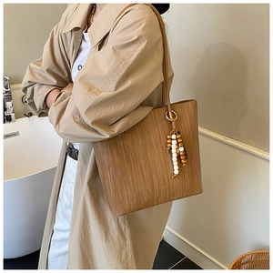 Dettaglio di una borsa tote marrone capiente con trama intrecciata e ciondolo in legno