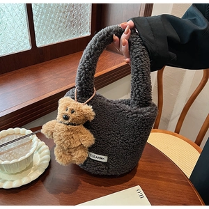 Détail du sac seau en peluche gris foncé avec pendentif ours mignon sur une table en bois