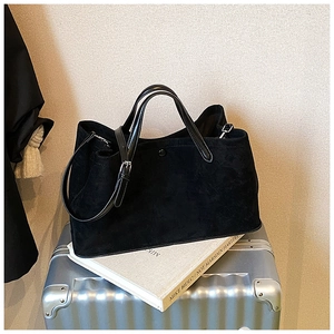 Detail of black matte suede tote bag with leather handles on a silver suitcase