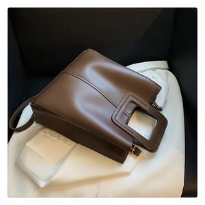 Detail of dark brown tote bag showing square cutout handle and gold hardware buckle