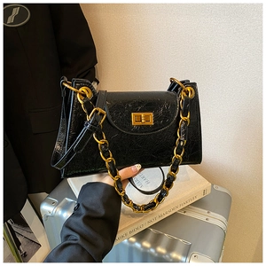 Close-up of black glossy chain bag with gold metal clasp and accordion side structure