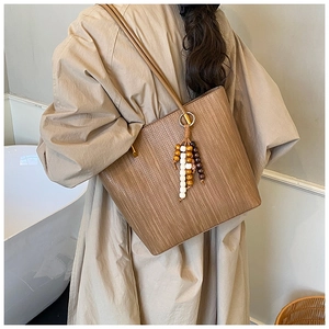 Dettaglio della borsa tote marrone intrecciata con ciondolo in legno e tracolla in pelle