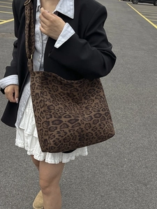 Large leopard print tote bag with wide strap worn over a black blazer and white skirt