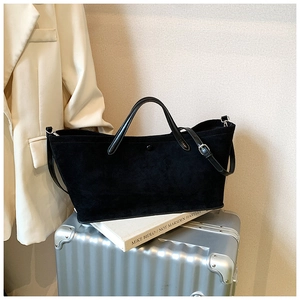 Detail of black suede tote bag with matte texture on silver suitcase in a travel setting
