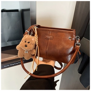 Détail d'un sac bandoulière vintage marron avec breloque chien peluche et plaque logo dorée