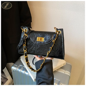 Close-up of black glossy patent leather shoulder bag with bold gold chunky chain strap