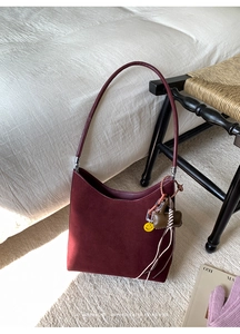 Detail of burgundy faux suede tote bag with signature smile charm and textured finish