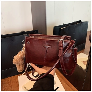 Détail d'un sac à main bordeaux en cuir verni avec un ours en peluche et logo en métal