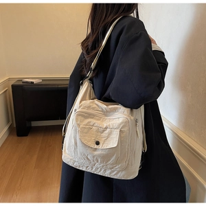 Detail of cream multi-pocket shoulder bag featuring durable nylon texture and metal zippers