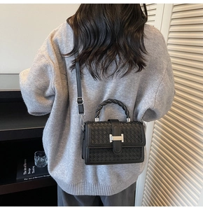 Detail of black woven leather square bag with braided handle and silver H-clasp