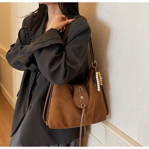 Detail of a brown suede tote bag with a vintage beaded pendant and metallic buckle