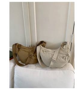 Minimalist nylon crescent crossbody bags in camel and beige colors on a white sofa