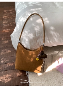 Close-up of brown suede tote bag with decorative charms on a soft minimalist background