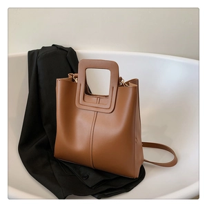 Detail of caramel brown tote bag with square handle and adjustable strap on white background