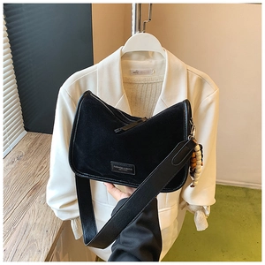 Detailansicht einer schwarzen Wildleder-Pillow-Bag mit Logo-Plakette und Holzperlen-Anhänger