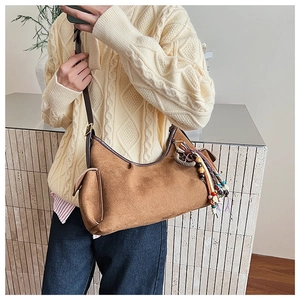 Detail of a brown suede crossbody bag with ethnic beaded charm and side pocket