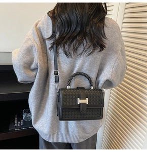 Close-up of black woven crossbody bag with silver H-shaped buckle and braided handle