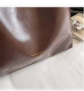 Close-up of soft brown leather tote bag with embossed brand logo and premium oil texture