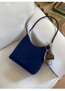 Detail of navy blue suede shoulder bag with retro charm and mini purse pendant on sofa