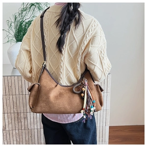 Detail of a brown suede hobo bag with a colorful ethnic fringe pendant and leather strap