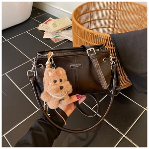 Détail du sac bandoulière en cuir noir brillant avec logo en métal et breloque chien