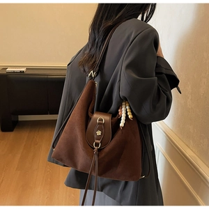 Close-up of dark brown suede tote featuring metal flower buckle and beaded charm detail