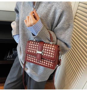 Detail of red-brown woven crossbody bag with silver buckle worn by a model