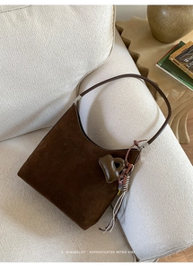 Detailed close-up of dark brown suede hobo bag with unique letter charm on cozy sofa