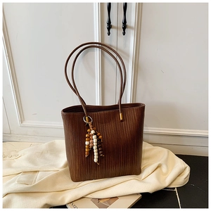Dettaglio borsa tote intrecciata marrone scuro con ciondolo in legno boho su tessuto beige