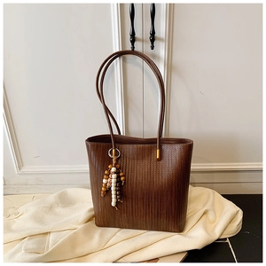 Dettaglio della borsa tote intrecciata marrone scuro con texture e ciondolo in perle di legno