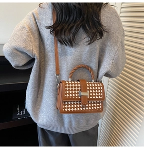 Detail view of woven leather bag with twist handle and metal H buckle on a shoulder strap