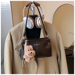Détail d'un sac porté épaule en cuir brillant marron foncé avec un charmant chiot en peluche