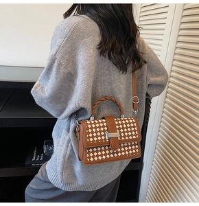Detail view of woven leather handbag with twisted handle and H-shaped metal buckle on model