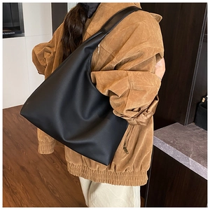 Detailed view of a large black matte hobo bag worn with a stylish autumn brown coat