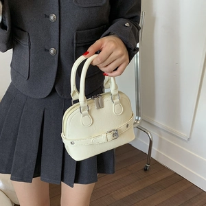 Detail of a chic cream shell bag with dual metal zippers and wrap-around buckle strap