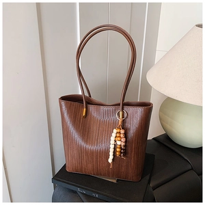 Dettaglio borsa tote marrone intrecciata con charm di perline vintage su espositore