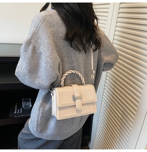 Close-up of cream woven square handbag with silver clasp and twisted handle texture