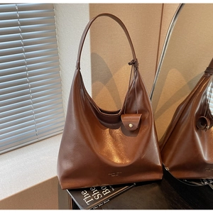 Détail d'un grand sac hobo en cuir marron montrant un logo doré sur une finition glacée