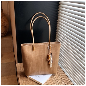 Dettaglio della borsa tote intrecciata kaki con spalline in pelle e ciondolo con nappe