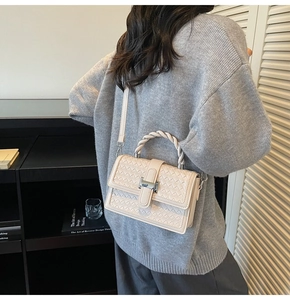 Detail of a beige woven leather handbag with a twisted handle and silver metal buckle