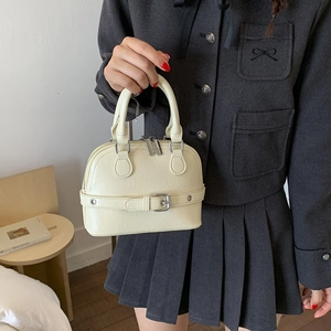 Detail of beige shell-shaped handbag showing glossy wrinkled leather and metal buckles
