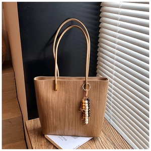 Dettaglio della borsa tote marrone intrecciata con un ciondolo di nappe in perle di legno