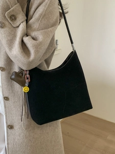 Large black suede tote bag with decorative charms worn by a model in a beige coat